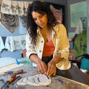 Woman carving a block in a room with various items on the wall and table.