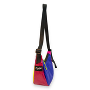 A multicolor Flowfold sling bag with a black shoulder strap, featuring a color-blocked design in pink, purple, and yellow, with a black brand patch on the front.