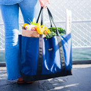 Person holding a blue reusable bag with groceries against a blurred background